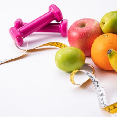 Fitness composition with pink dumbbells, fresh fruits, and measuring tape on a white background A fitness composition with pink dumbbells, fresh fruits, and measuring tape on a white background